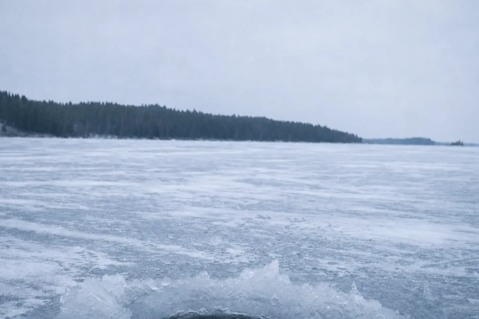 Isbelagd sjö med ett upptaget ishål i förgrunden